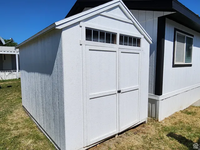 Detached storage shed with a gable roof, white panel siding, and upper transom windows