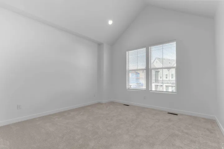 Vaulted ceiling with recessed lighting, dual windows with blinds, and neutral carpeting