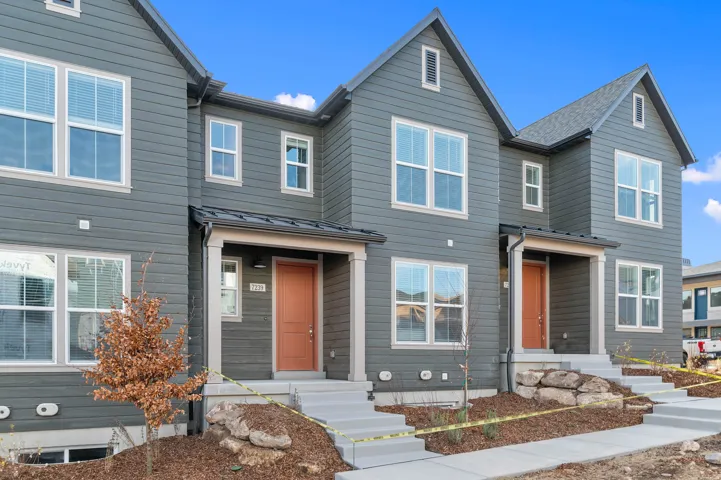 Modern townhome exterior featuring gray horizontal siding, white trim, a covered porch, and an orange entry door