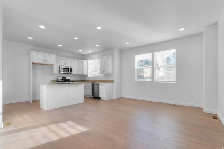 Wood-finish flooring, recessed lighting, white cabinetry, stainless steel appliances, and a kitchen island