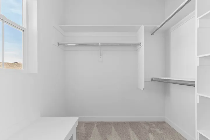 White built-in shelving, chrome hanging rods, window with white trim, white built-in bench, and light grey carpet flooring