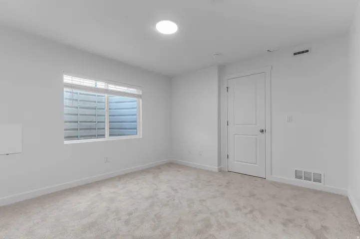 Neutral wall paint, light-toned carpet, recessed circular ceiling light, white window blinds, and a white two-panel interior door