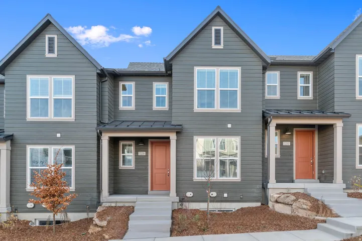 Contemporary townhome exterior featuring horizontal siding, white-trimmed windows, a covered front porch, and a contrasting entry door