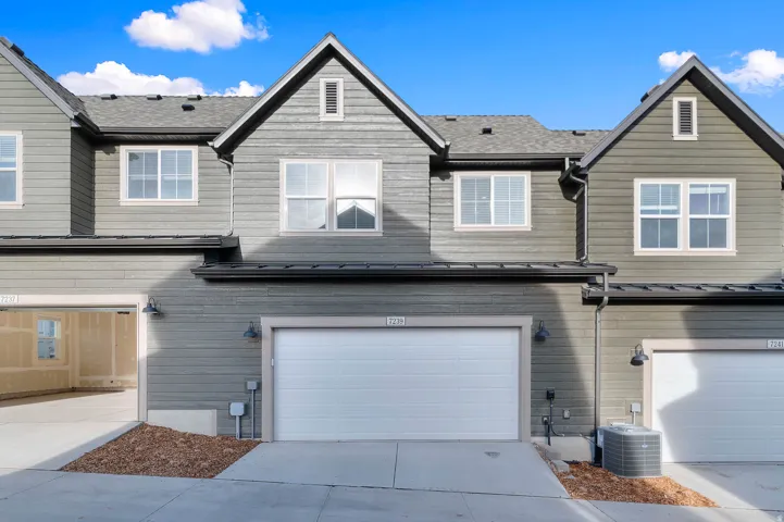Modern townhome featuring gray horizontal siding, white-framed windows, and an attached garage with a white door