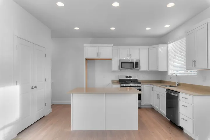 Modern kitchen featuring white cabinetry, light countertops, stainless steel appliances, and wood-finish flooring