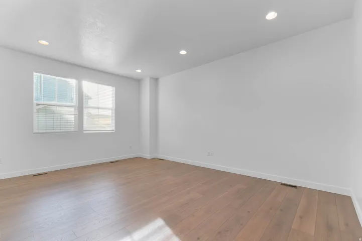 Recessed lighting, wood-finish flooring, two windows with blinds, and white painted walls