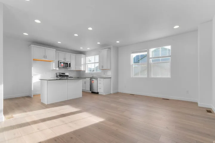 Open-concept living space with light wood-finish flooring, recessed lighting, and large windows