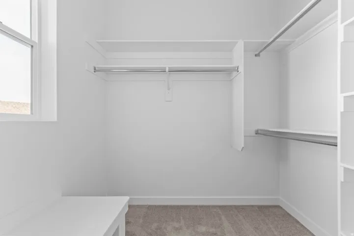 Walk-in closet featuring built-in shelving, chrome hanging rods, a window, and a built-in bench