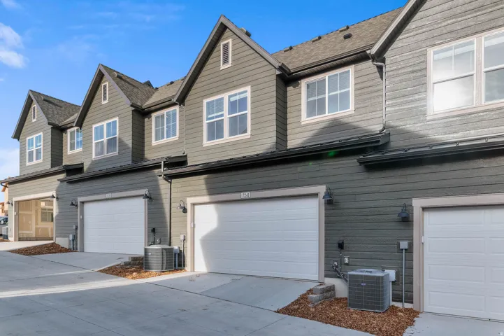Modern townhome exterior featuring gray siding, white-trimmed windows, attached garages with white doors, and gabled rooflines