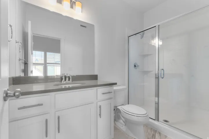 White vanity with a single basin, grey countertop, and chrome faucet