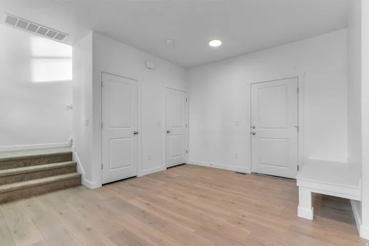 Light wood-finish flooring, recessed ceiling lighting, built-in storage bench, and carpeted stairs with white risers
