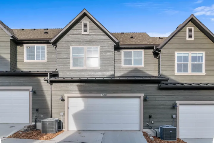Multi-level property exterior with horizontal siding, gabled rooflines, and individual garage doors