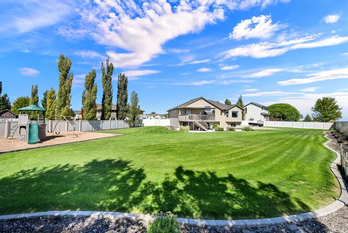 Expansive backyard with a manicured lawn, dedicated play area, and a tiered retaining wall