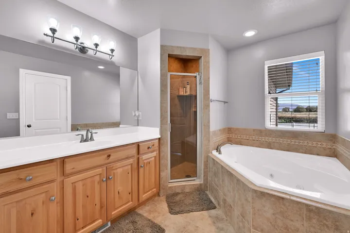 Corner soaking tub, glass-enclosed shower, wood-finish vanity with dual sinks, and tile flooring