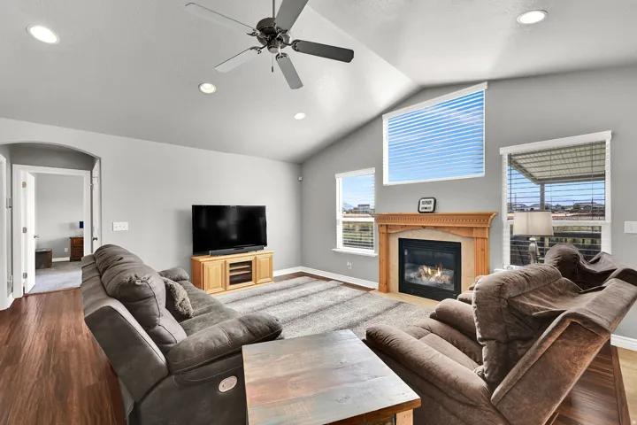 Vaulted ceiling with recessed lighting and a ceiling fan, gas fireplace with a wood-finish mantel, and wood-finish flooring