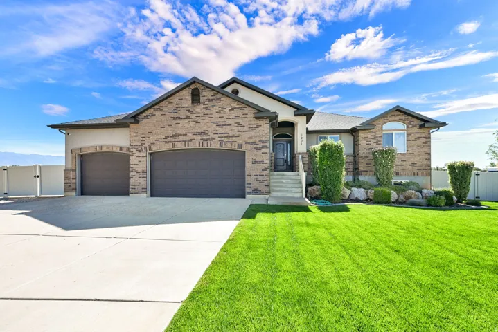 Exterior featuring a brick and stucco facade, an arched entry, two arched garage doors, a concrete driveway, and a manicured lawn