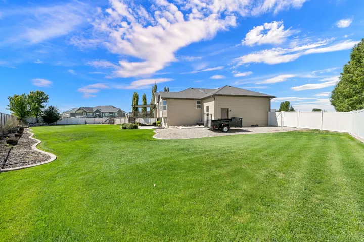 Expansive grassy lawn with a white privacy fence, multi-level deck, and landscaped rock beds