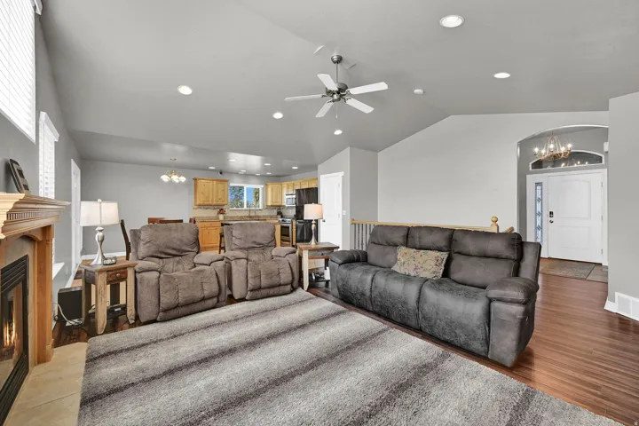 Vaulted ceiling with recessed lighting, wood-finish flooring, fireplace with wood mantel, white paneled entry door with transom and side lights, and a kitchen with wood cabinetry