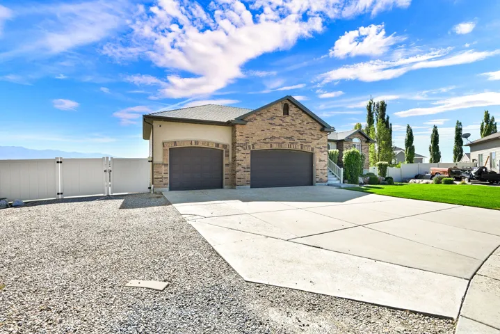 Two-car garage with arched doors, brick and stucco exterior, concrete driveway, and gravel side yard