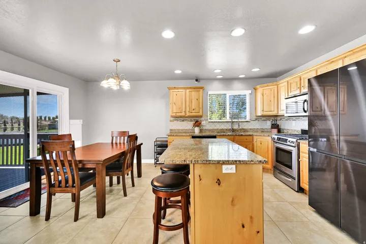 Kitchen featuring light wood cabinetry, granite-finish countertops, stainless steel appliances, and a tile backsplash
