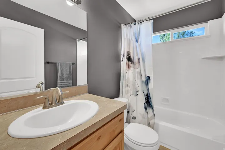 Bathroom featuring a single vanity with an oval sink, brushed nickel faucet, light wood-finish cabinetry, and a white tub/shower combination