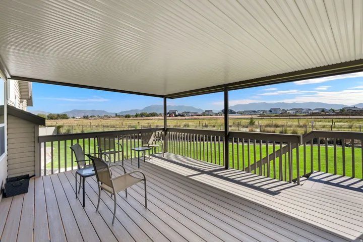 Covered outdoor deck with composite decking and wood railing, overlooking an expansive green space with distant mountain ranges