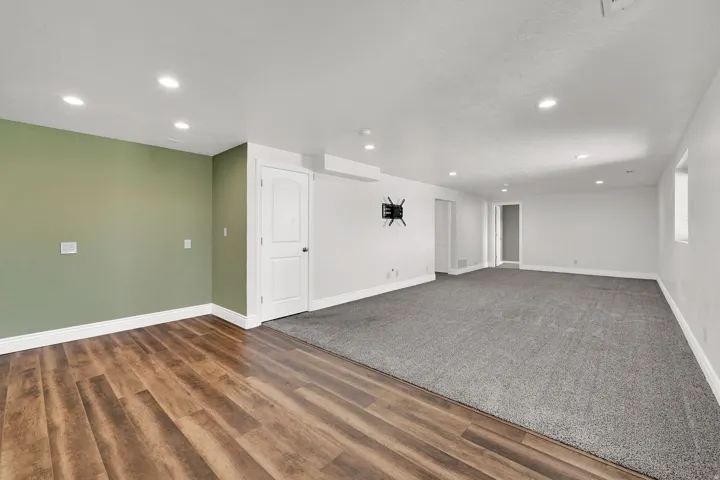 Recessed lighting, wood-finish flooring, light green accent wall, white painted walls, gray carpeting