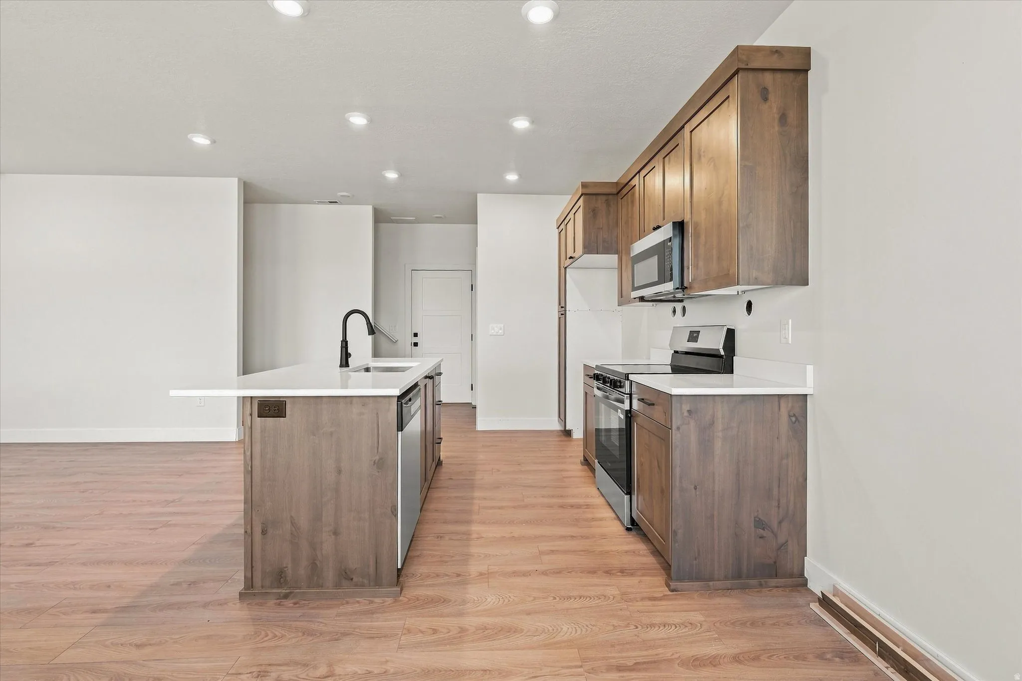 Kitchen featuring wood-finish flooring, recessed lighting, wood cabinetry, a center island with a sink, and stainless steel appliances