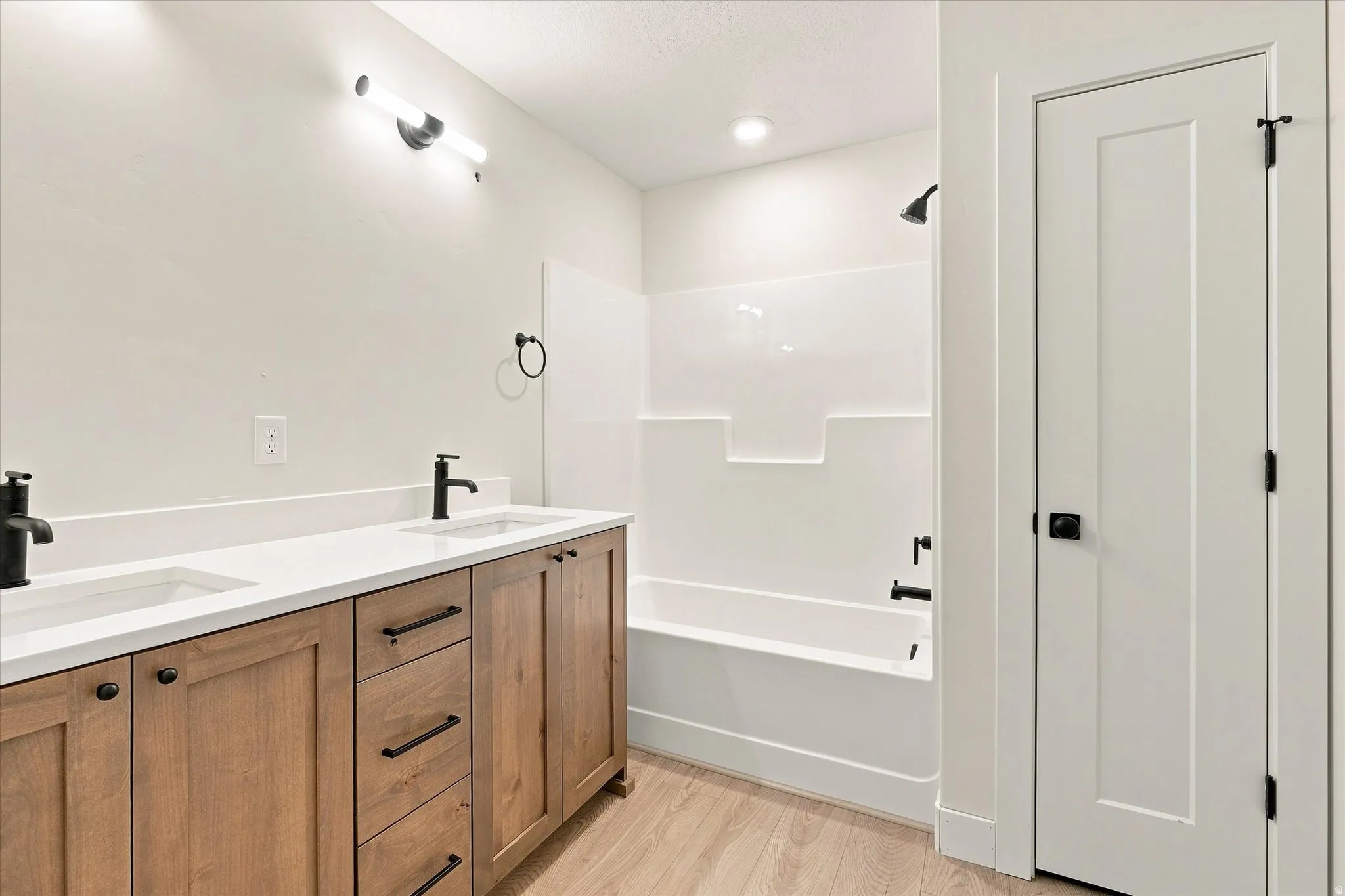 Dual vanity with wood-finish cabinetry, white solid-surface countertop, and matte black fixtures