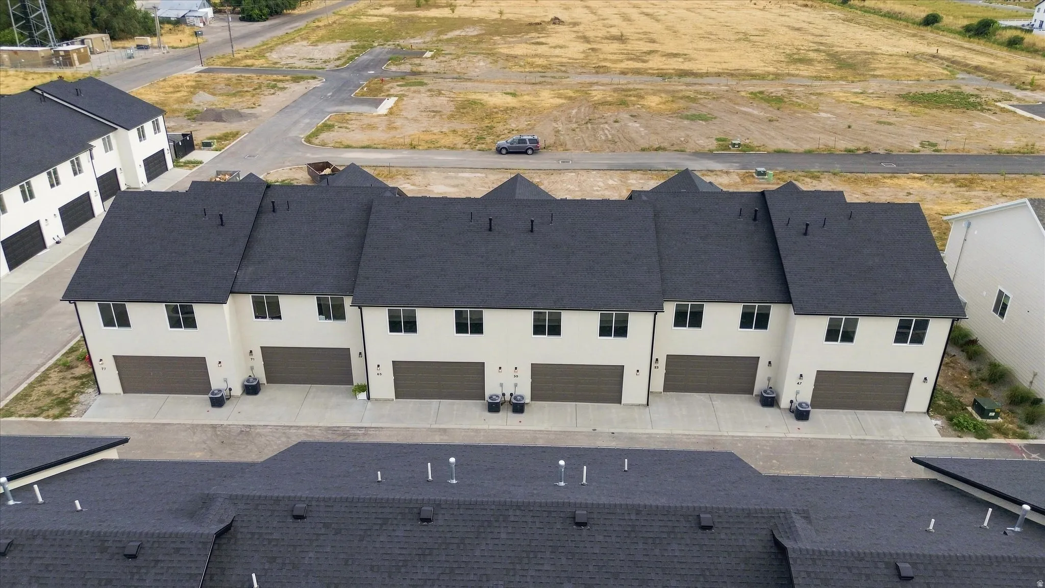 Townhome residences featuring light-toned siding, dark roofing, and attached garage doors