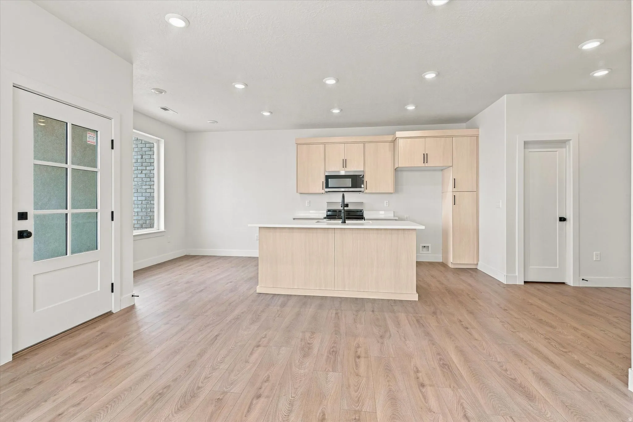 Open-concept living space with wood-finish flooring, recessed lighting, a kitchen island, and light wood cabinetry