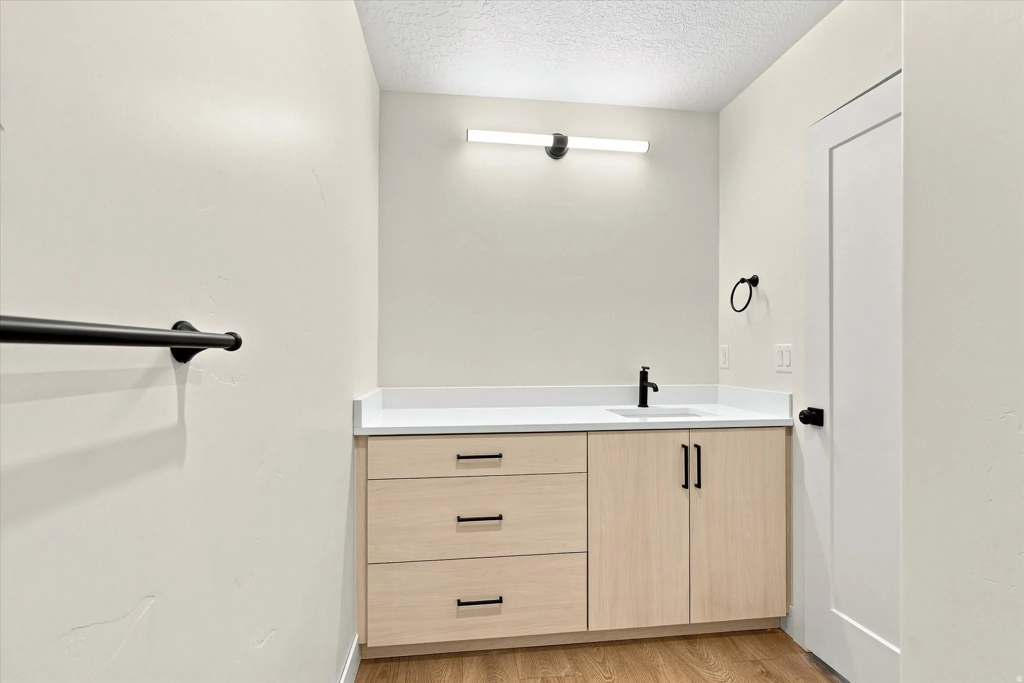 Vanity with light wood-finish cabinetry, white countertop, and matte black fixtures
