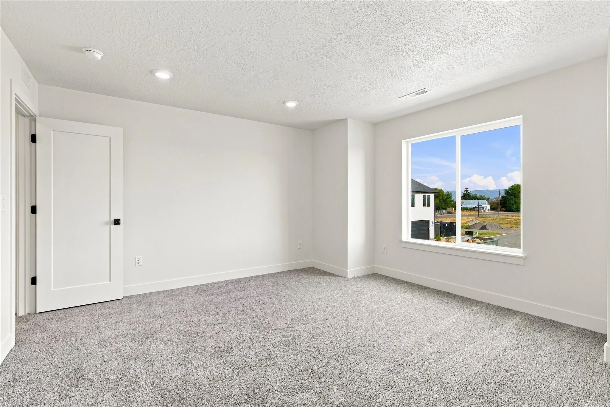 Recessed ceiling lighting, white interior door with black hardware, large window, gray carpet, and white trim