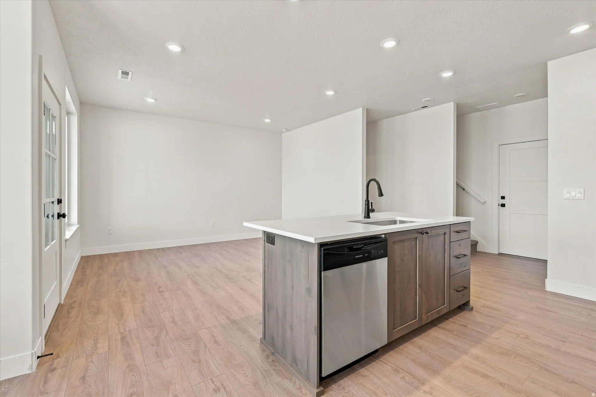 Kitchen island with a white countertop and dark wood-finish cabinetry, integrated stainless steel dishwasher, and a matte black gooseneck faucet