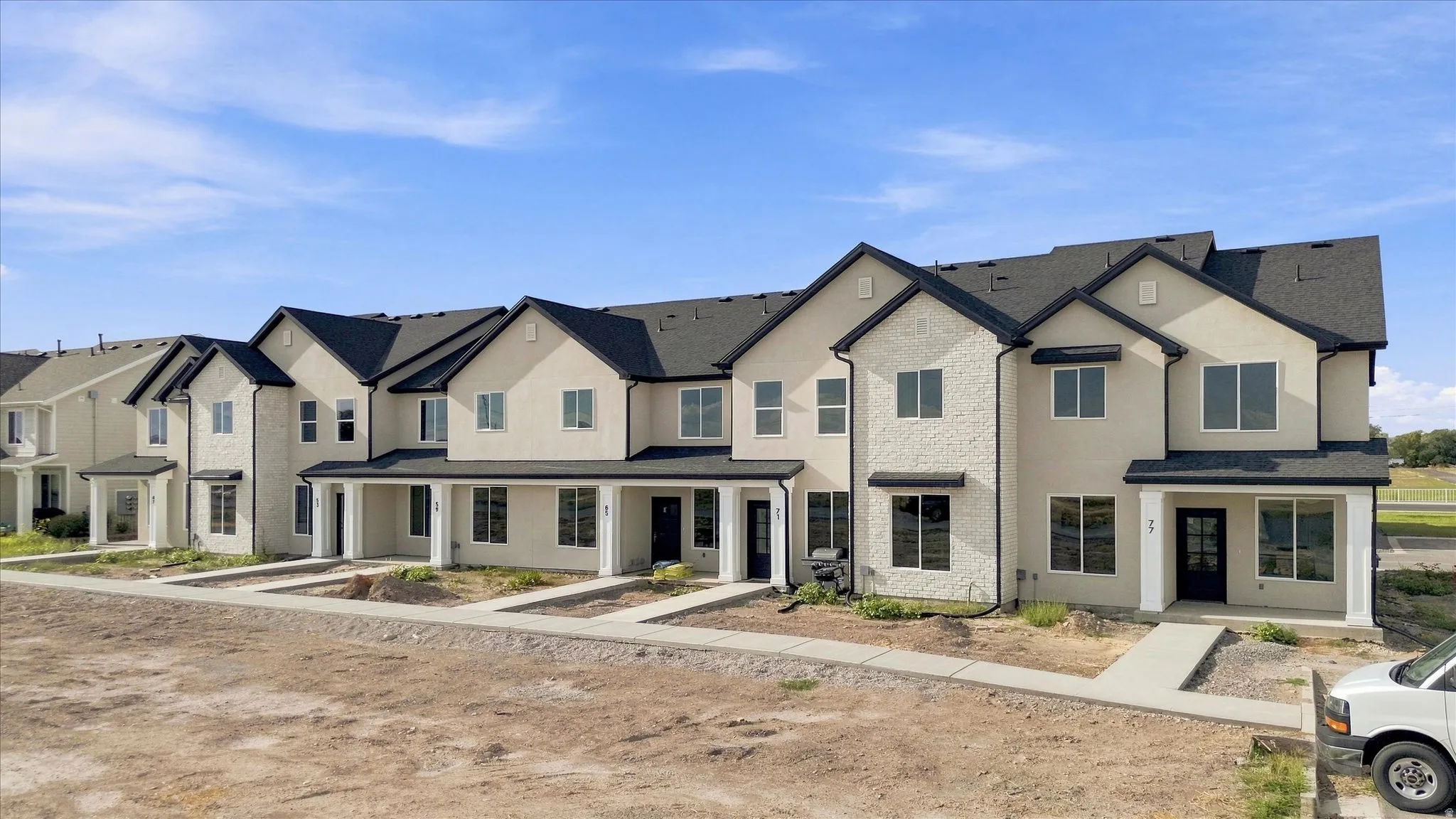 Contemporary multi-level townhome architecture with dark shingle roofing, stucco siding, and multiple large windows