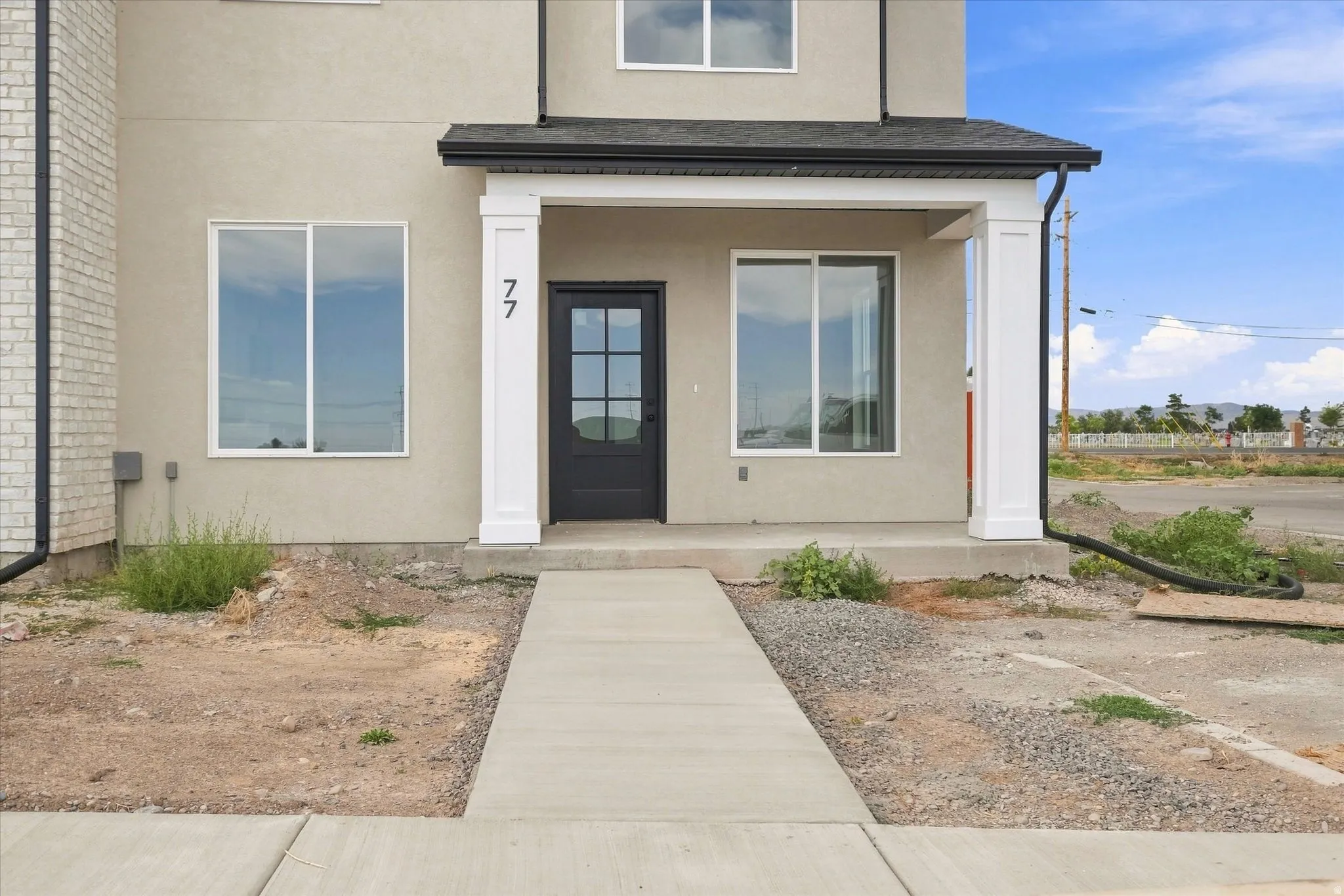 Stucco exterior with brick detailing, covered entry with white columns, and a black entry door with windowpanes