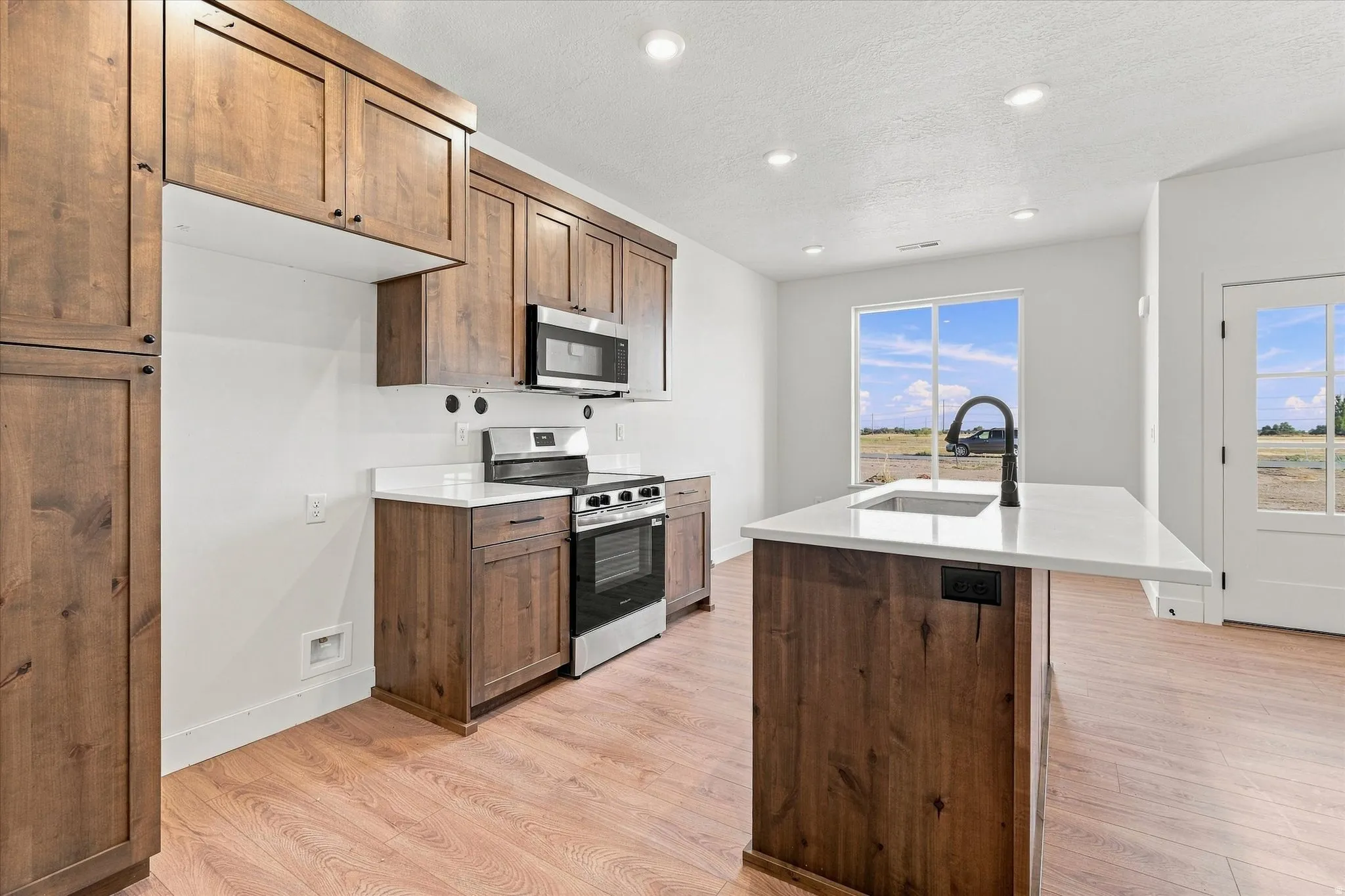 Kitchen featuring wood-finish cabinetry, stainless steel appliances, white countertops, and wood-finish flooring