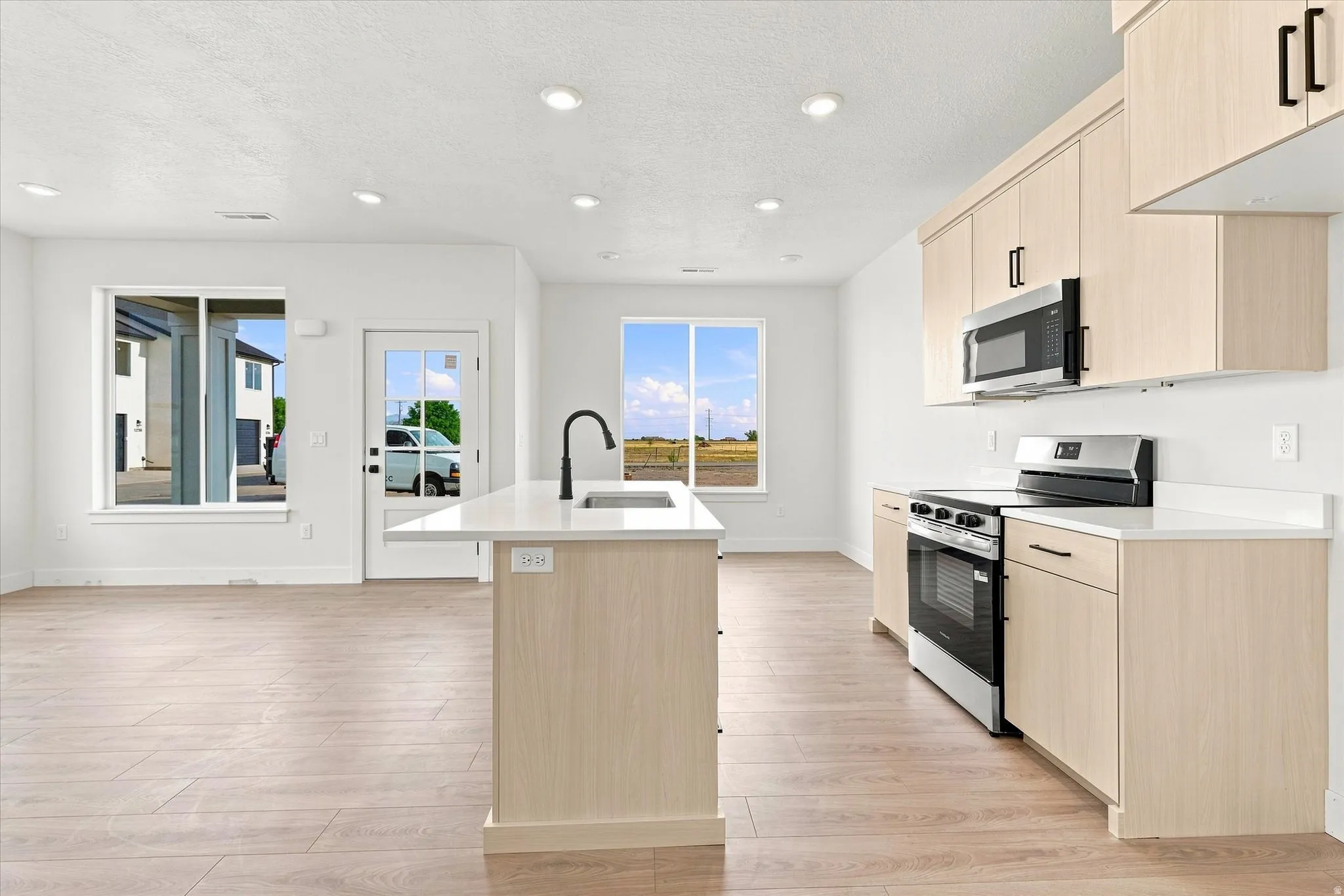 Open concept living space featuring wood-finish flooring, recessed lighting, a kitchen island with a sink, white countertops, and light wood-finish cabinetry