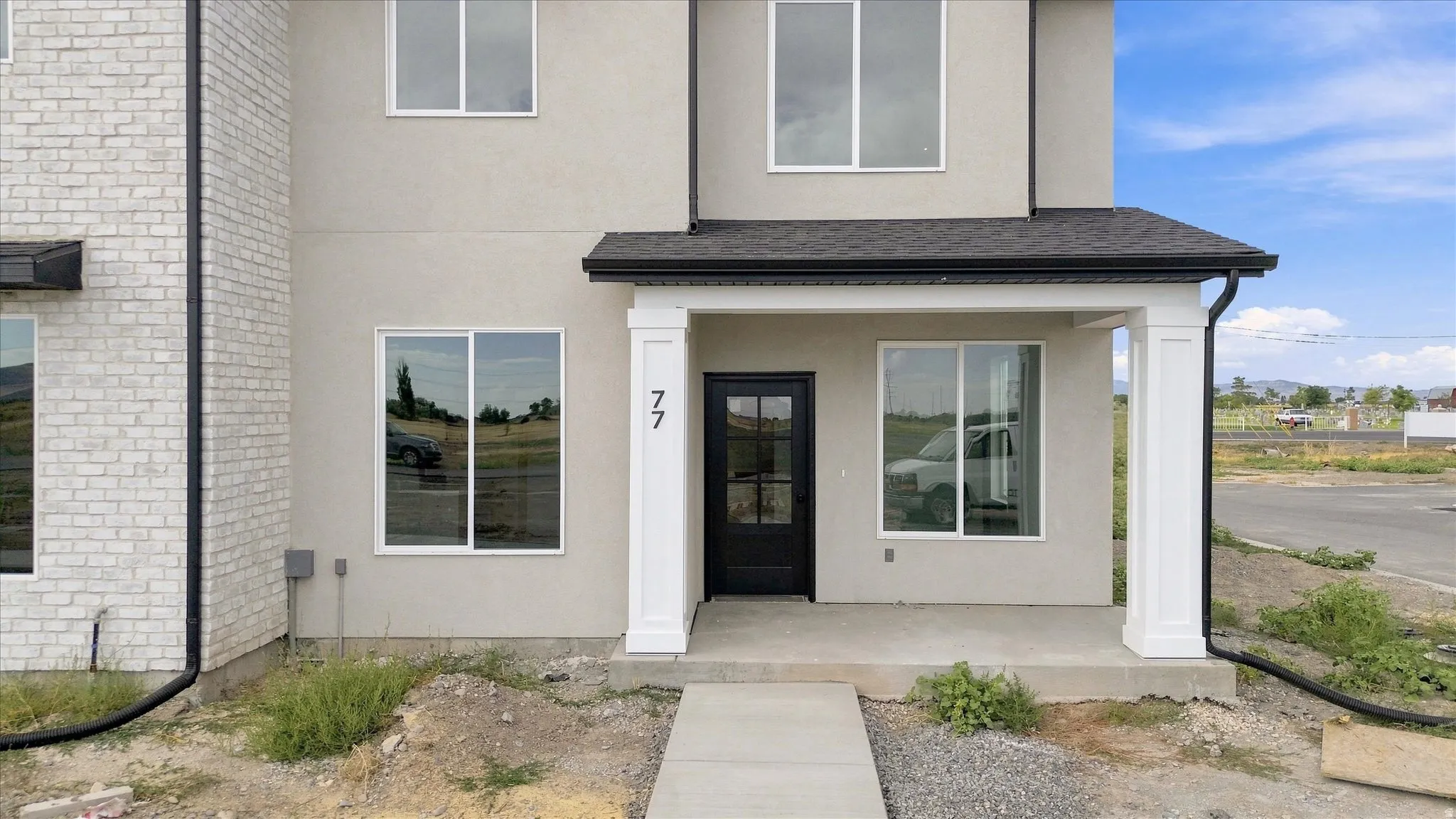 Two-story stucco and brick exterior featuring a black front door, white window frames, and a covered porch with white columns