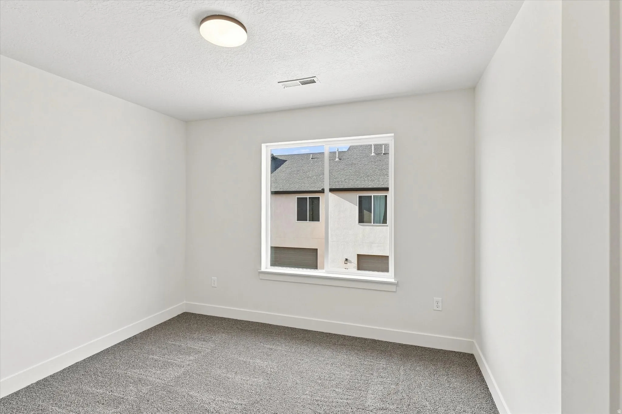 Neutral wall paint, textured carpet, window with white trim, and a flush-mount ceiling light