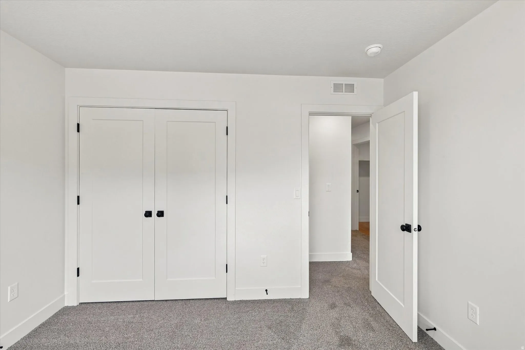 Light-colored carpet, white walls, white trim, and white doors with matte black hardware