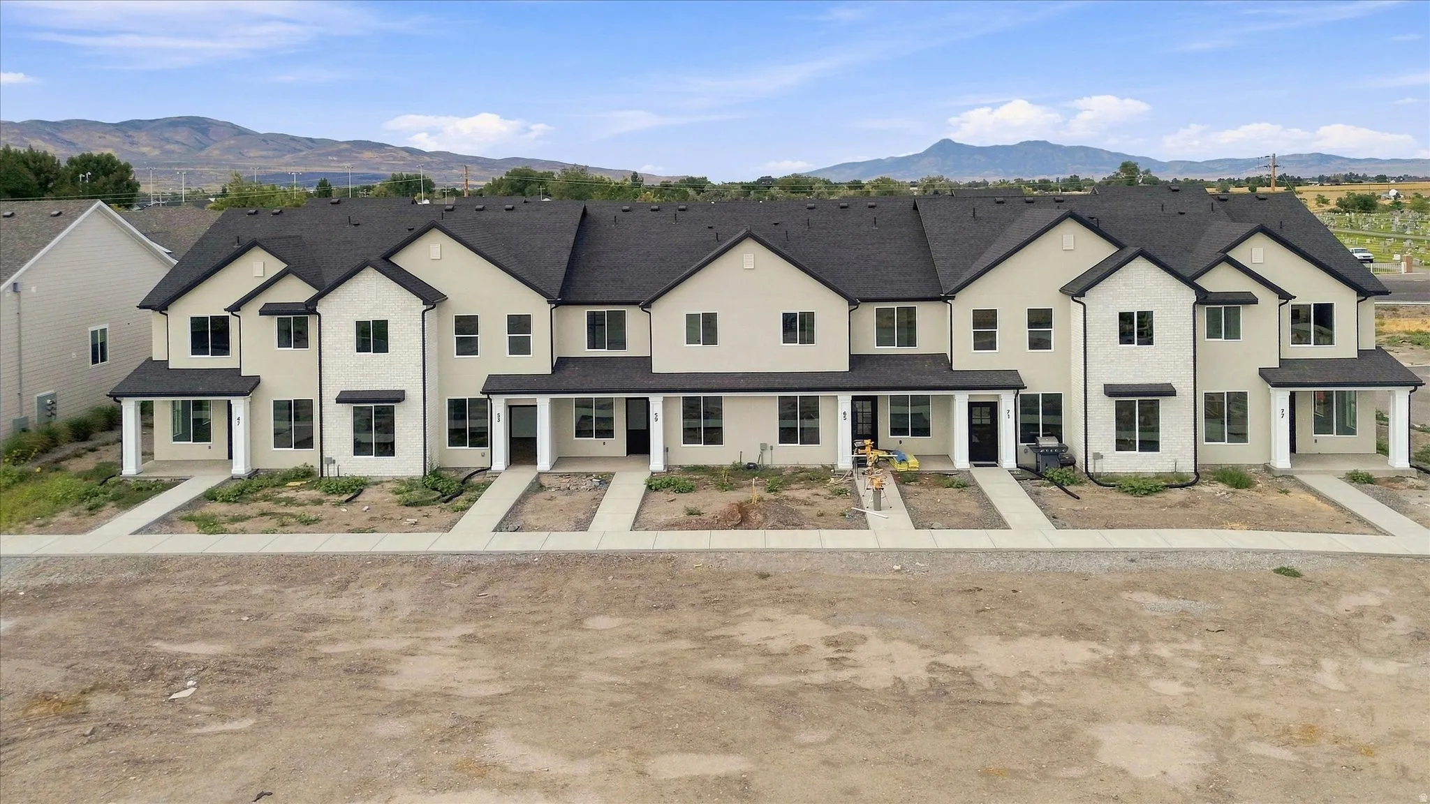 Modern townhome exteriors featuring light-colored siding, dark shingle roofing, and covered entryways