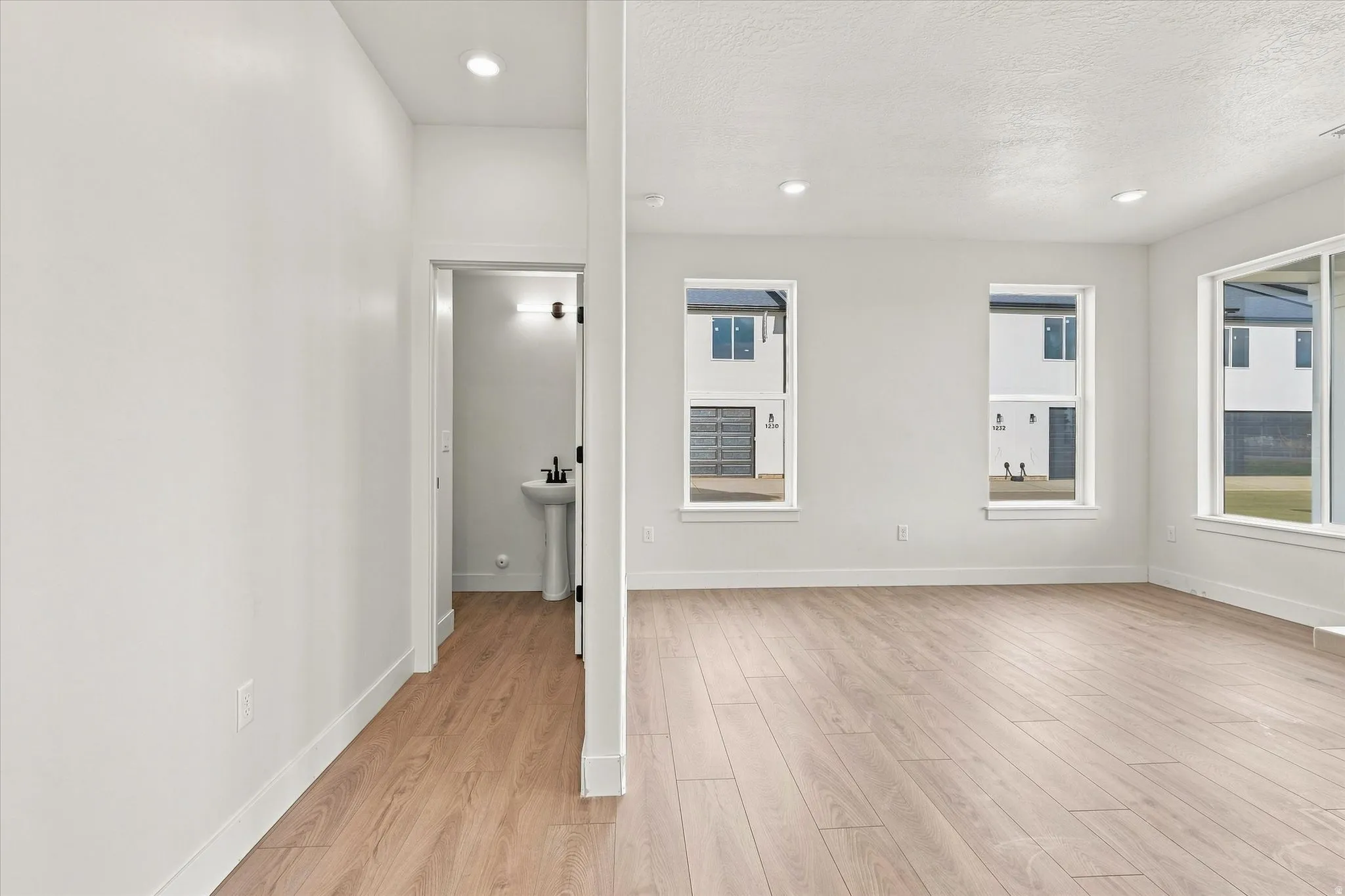 Recessed lighting, wood-finish flooring, multiple windows, and a pedestal sink with a matte black faucet