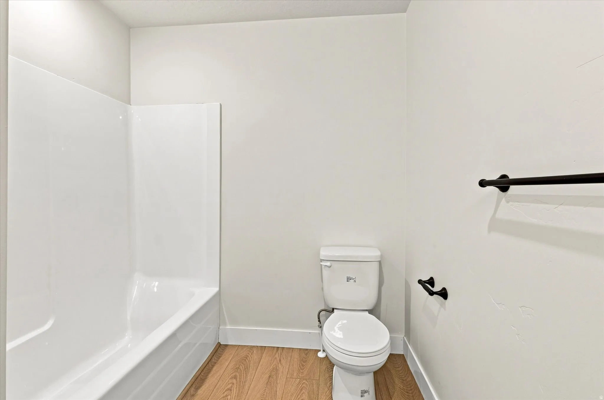 White fiberglass tub/shower combination, white toilet, wood-finish flooring, and matte black hardware
