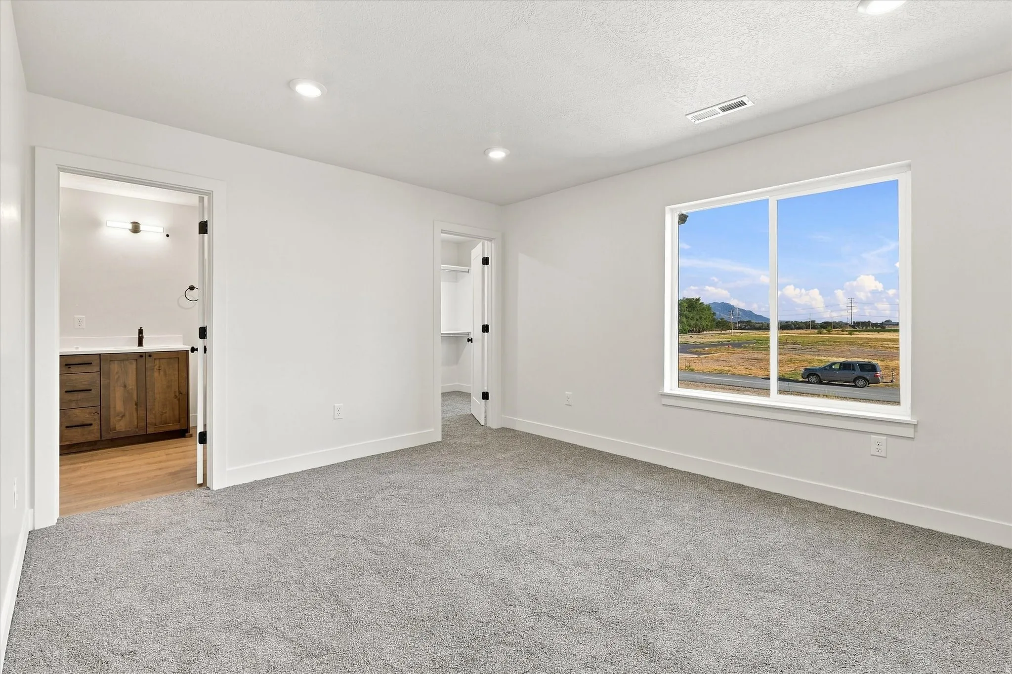 Spacious room with gray carpeting, white walls, recessed lighting, and a large window