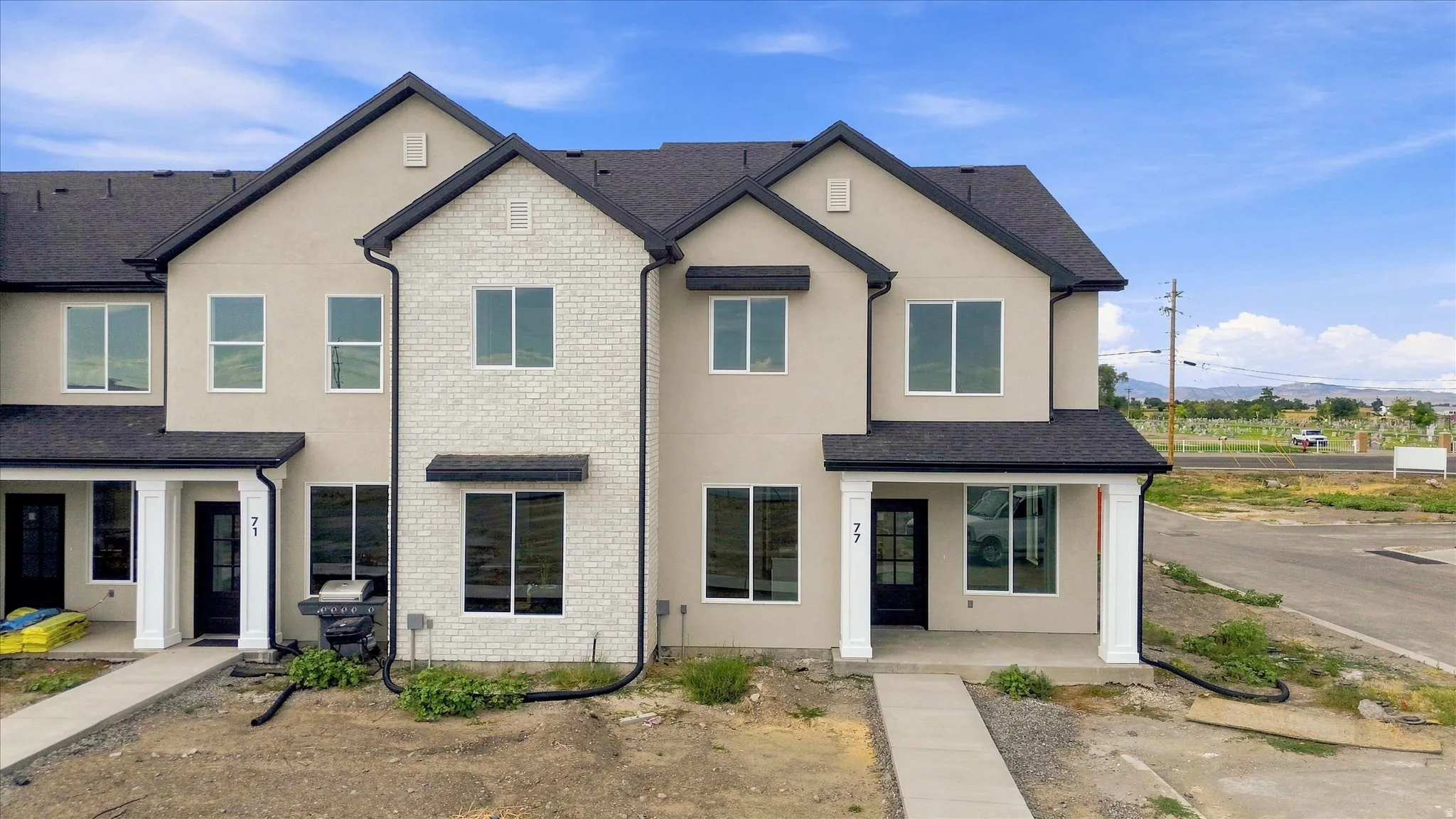 Contemporary townhome featuring a stucco and white brick facade, dark shingle roof, and white-framed windows