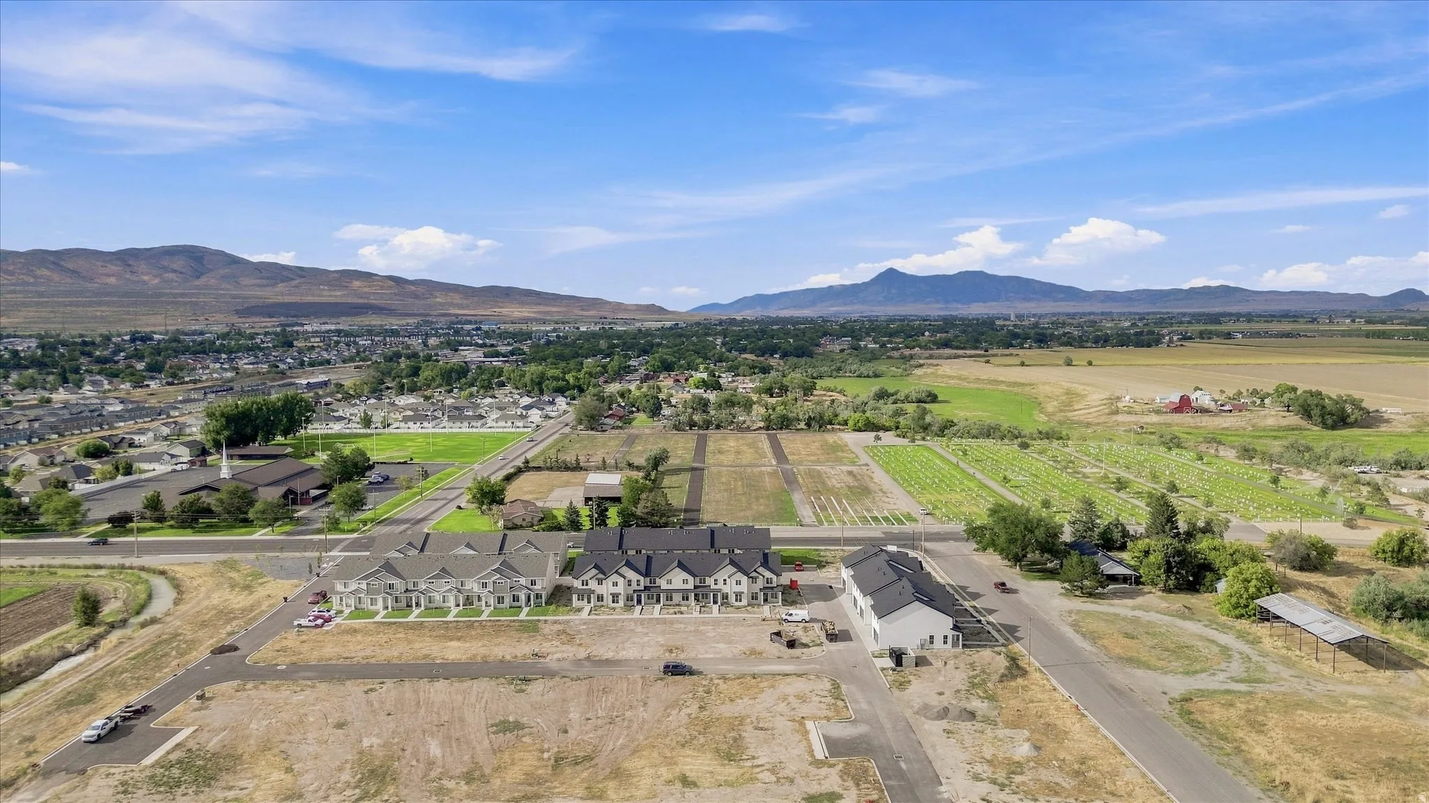 Developing residential area with mountain backdrop, established green spaces, and adjacent agricultural land