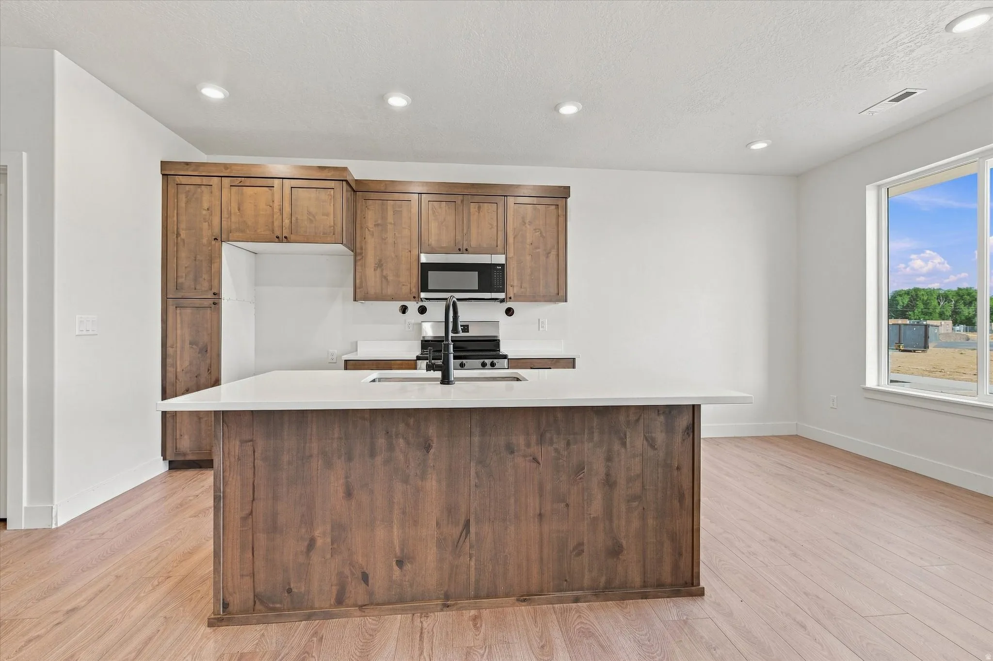Kitchen featuring a center island with a light-colored countertop, wood-finish cabinetry, built-in microwave, and a window providing natural illumination