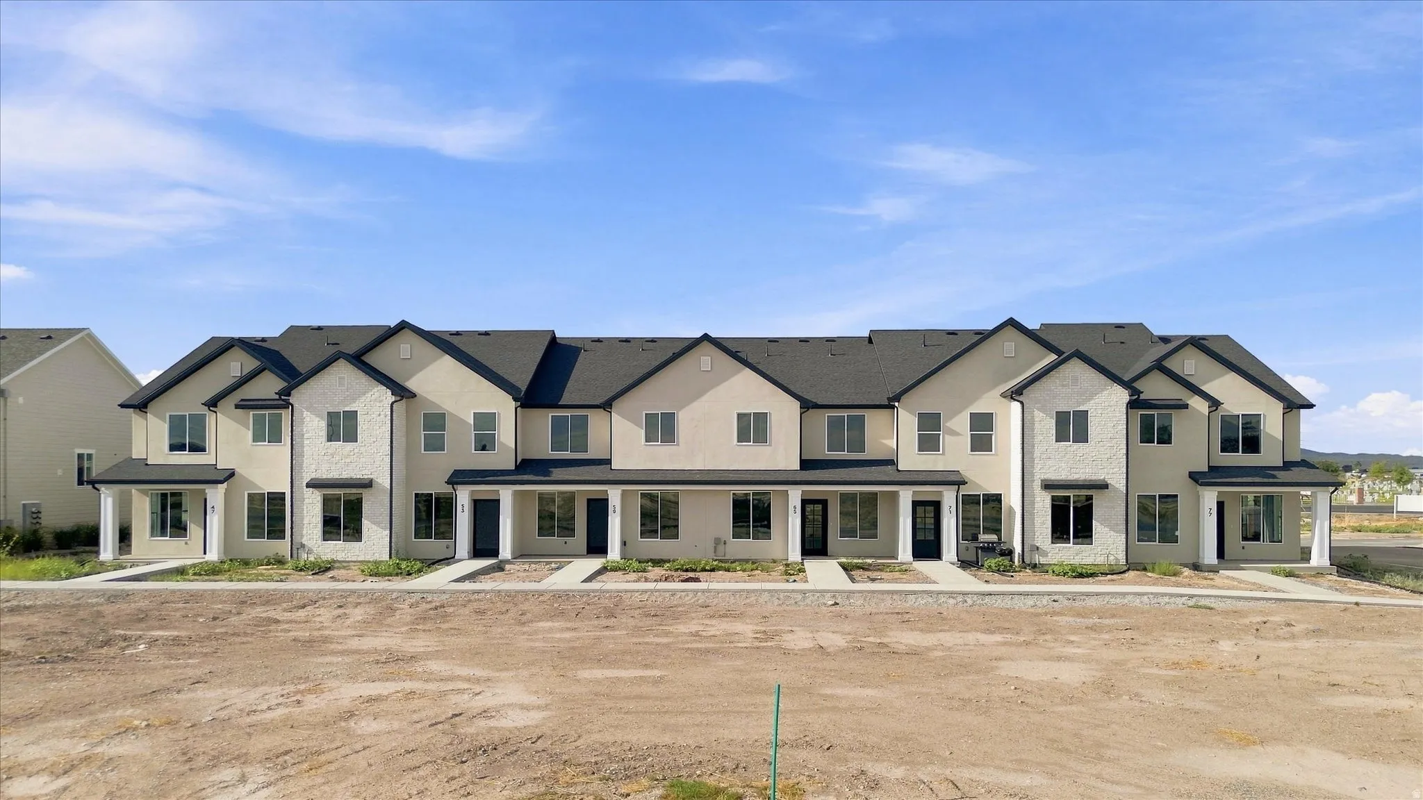 Contemporary townhome exteriors featuring light-toned stucco and dark rooflines