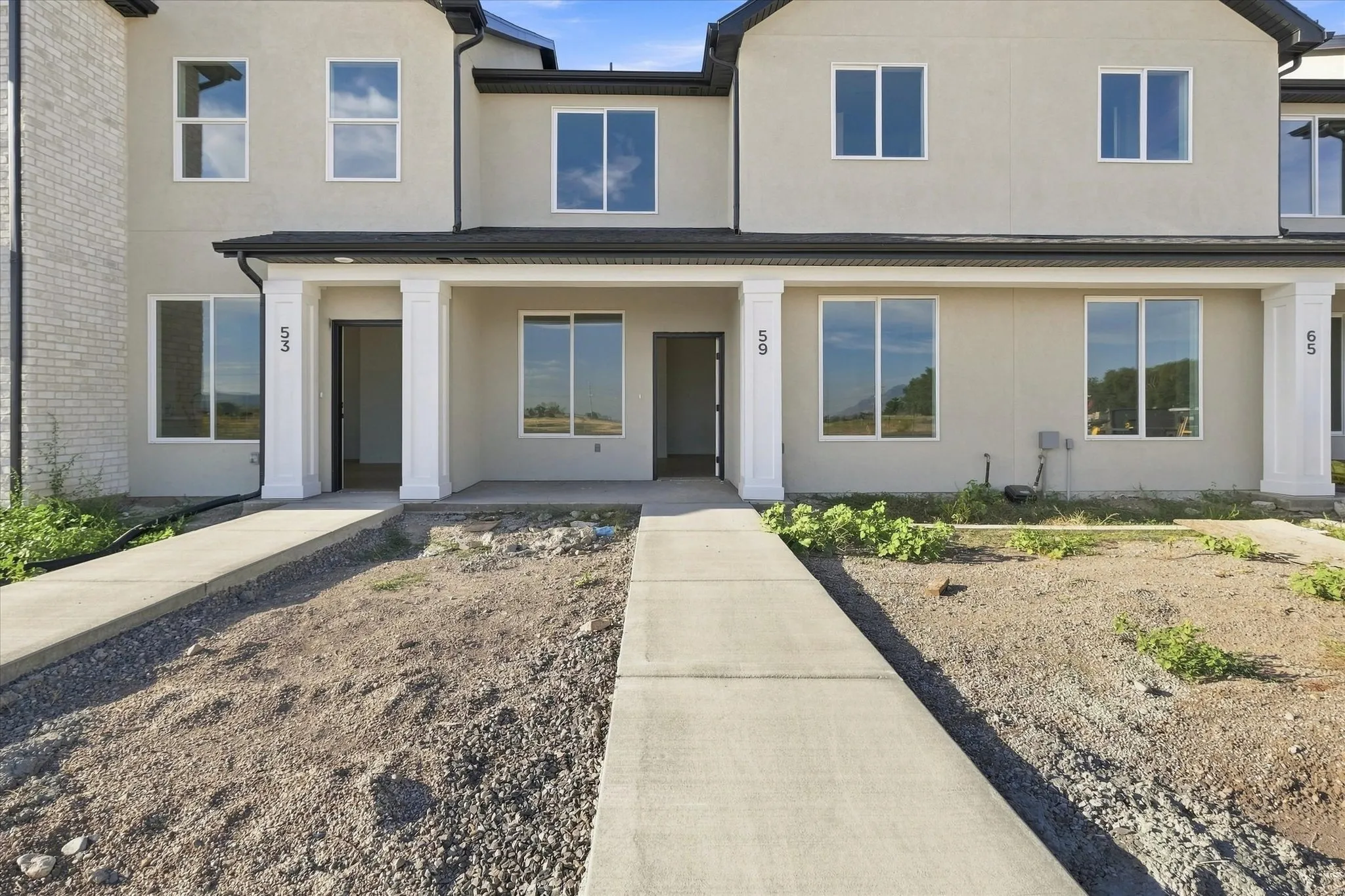 Stucco exterior, covered entryways, multiple large windows, and concrete walkways